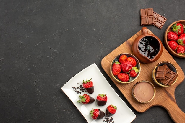 Draufsicht aus der Ferne Schokolade an Bord mit Schokolade überzogene Erdbeeren auf Teller neben dem Schneidebrett mit Schokoladencreme und Erdbeeren und Schokoladentafeln