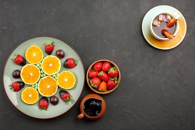 Draufsicht aus der ferne schokolade und früchte gehackte orange schokoladenüberzogene erdbeergrüne bonbons und schalen mit schokoladensauce und erdbeeren und eine tasse tee mit zimtstangen