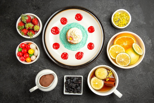 Kostenloses Foto draufsicht aus der ferne süßigkeiten mit teeteller mit appetitlichem cupcake neben der tasse kräuterteeschalen mit schokoladencreme-erdbeeren, zitrusfrüchten und bonbons