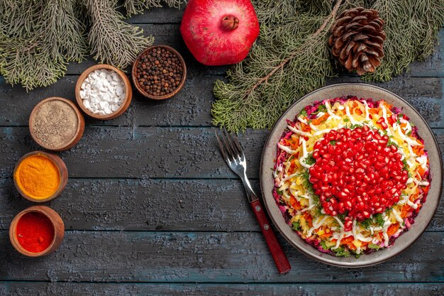 Draufsicht aus der Ferne Teller und Äste appetitlicher Teller mit Granatapfelkartoffeln neben den Schüsseln mit Gewürzgabel Granatapfel und Äste mit Zapfen auf dem Tisch