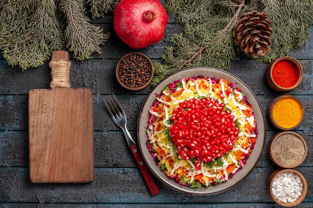 Draufsicht aus der Ferne Teller und Äste Granatapfel neben der Gabel Schüsseln mit Gewürzen Granatapfel Schneidebrett und Äste mit Zapfen