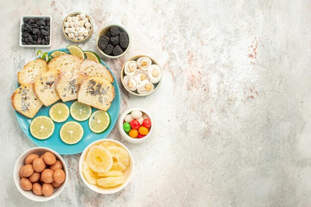 Draufsicht aus der Ferne Zitronenkuchen sieben Schüsseln mit Bonbons neben dem Teller mit Kuchenstücken mit Zitrone auf dem Tisch