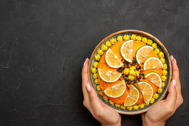 Draufsicht aus der Ferne Zitrusfrüchte und Schokoladen-Orangenkuchen mit Schokolade in den Händen auf dem schwarzen Tisch