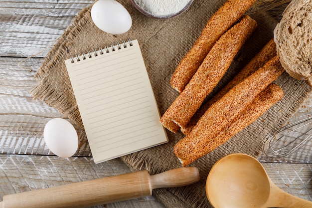 Draufsicht Bäckerei mit Notizblock, Eiern, Nudelholz auf Sackleinen und Holzoberfläche. horizontal