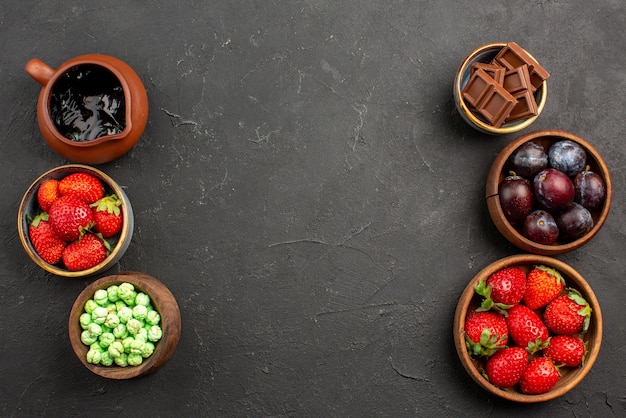 Draufsicht beeren und süßigkeiten schokoladensauce erdbeeren schokolade grüne bonbons und beeren in braunen schalen auf dem tisch