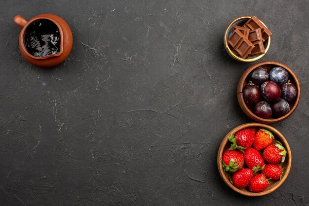 Draufsicht Beeren und Süßigkeiten Schokoladensauce Erdbeeren Schokolade und Beeren in braunen Schalen auf dem dunklen Tisch