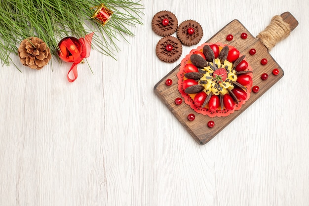 Draufsicht-Beerenkuchen auf den Schneidebrettplätzchen und den Kiefernblättern mit Weihnachtsspielzeug auf dem weißen Holzgrund