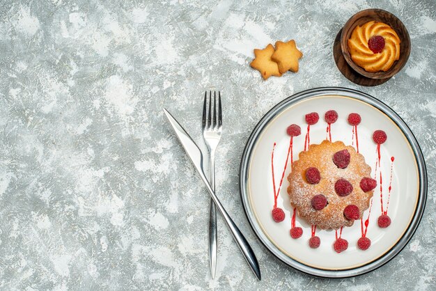Draufsicht Beerenkuchen auf weißem ovalem Plattenkeks in Schüssel gekreuzte Gabel und Abendessenmesser auf grauer Oberfläche freier Raum
