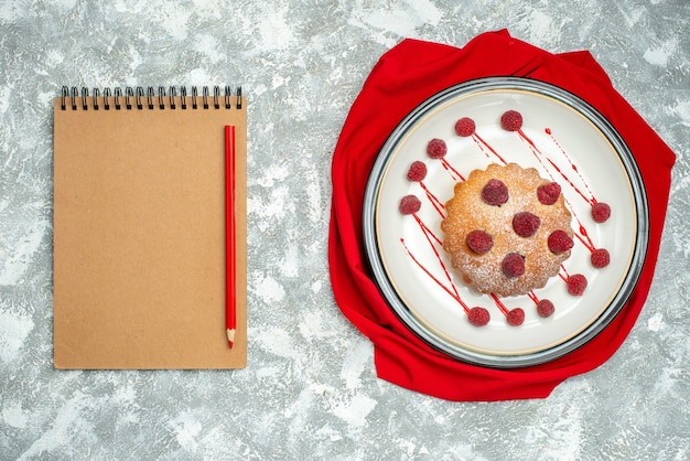 Draufsicht-Beerenkuchen auf weißem ovalem Tellerrotschalrotstift auf Notizbuch auf grauer Oberfläche