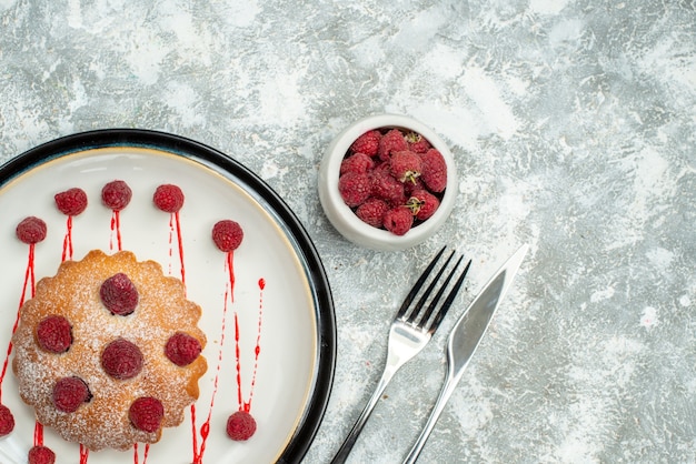 Draufsicht Beerenkuchen auf weißen ovalen Teller Himbeeren in Schüssel Gabel und Abendessen Messer auf grauer Oberfläche freien Raum