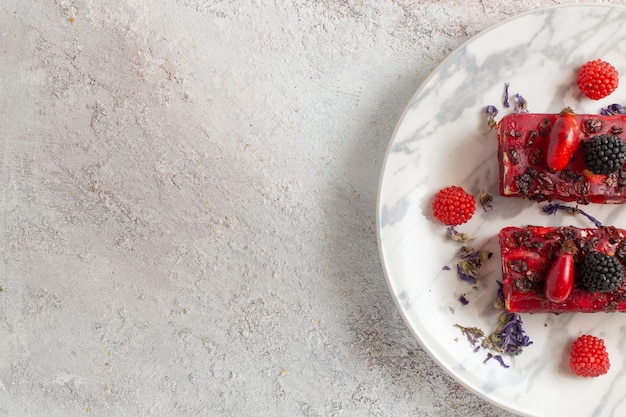 Draufsicht Beerenkuchenscheiben mit roter cremiger Glasur und frischen Beeren auf weißer Oberfläche