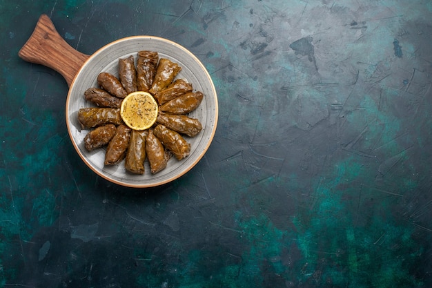 Kostenloses Foto draufsicht blatt dolma köstliche östliche fleischmahlzeit, die innerhalb der grünen blätter auf dem dunkelblauen schreibtischfleischmahlzeitnahrungsmittelessen-gemüsegesundheitskalorie gerollt wird