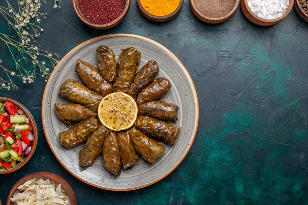 Draufsicht Blatt Dolma köstliche östliche Fleischmahlzeit gerollt in grünen Blättern mit Gewürzen und geschnittenem Gemüse auf dem blauen Schreibtisch Fleisch Abendessen Gericht Mahlzeit Mahlzeit