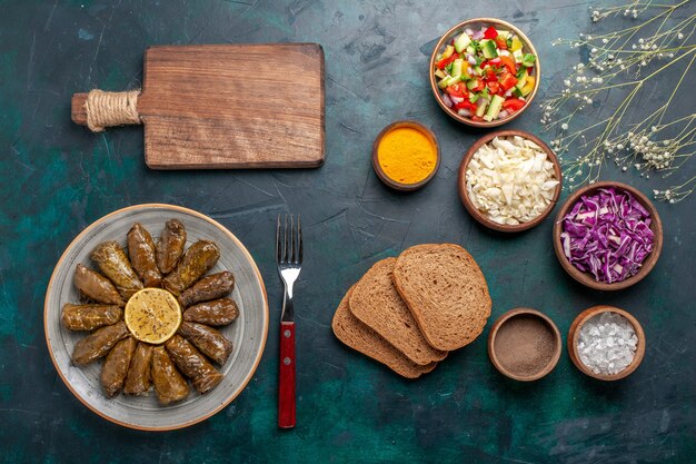 Kostenloses Foto draufsicht blatt dolma östliches fleischmehl gerollt in grünen blättern mit geschnittenem gemüse und brot auf ostmahlzeitmahlzeit des blauen schreibtischfleischs