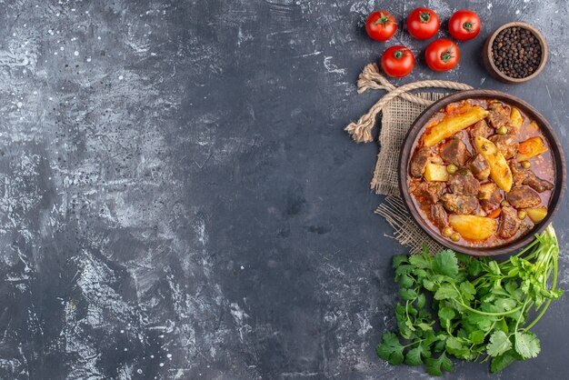 Draufsicht Bozbash-Fleischsuppe in Holzschale Koriandertomaten schwarzer Pfeffer in kleiner Schüssel auf grauem Tisch mit Kopierraum