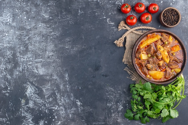 Draufsicht Bozbash-Fleischsuppe in Holzschale Koriandertomaten schwarzer Pfeffer in kleiner Schüssel auf grauem Tisch mit Kopierraum