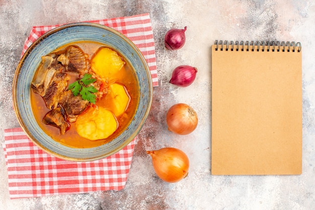 Draufsicht Bozbash Suppe Küchentuch gelbe und rote Zwiebeln ein Notizbuch auf nacktem Hintergrund