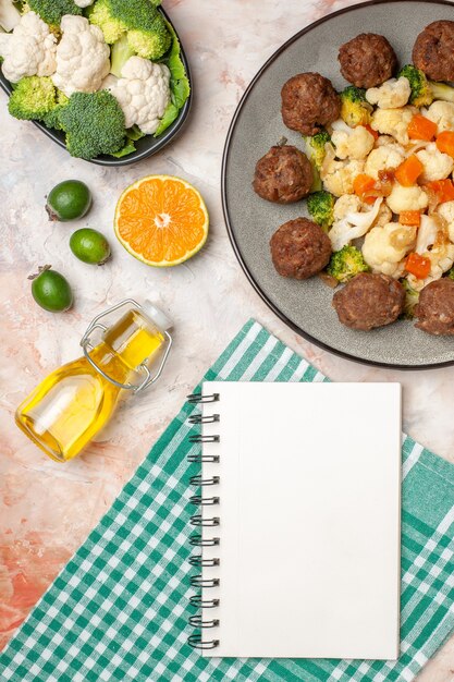 Kostenloses Foto draufsicht brokkoli und blumenkohlsalat und fleischbällchen auf teller kariertes serviettenöl rohes gemüse auf teller zitronenscheibe feykhoas ein notizblock auf nacktem, isoliertem hintergrund