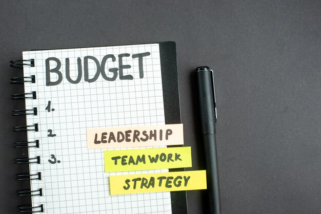 Draufsicht Budgetnotiz im Notizblock mit Stift auf dunkler Oberfläche Strategie Geschäftsmarketing Teamarbeit Büroführung Job Erfolg
