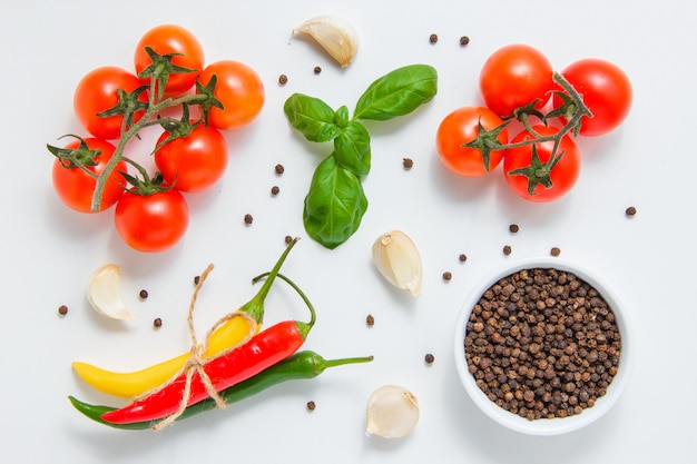 Draufsicht-Bündel von Tomaten mit einer Schüssel des schwarzen Pfeffers, des Knoblauchs, der Blätter, des Chilipfeffers auf weißem Hintergrund. horizontal