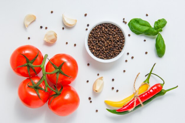 Draufsicht-Bündel von Tomaten mit einer Schüssel des schwarzen Pfeffers, des Knoblauchs, der Blätter, des Chilipfeffers auf weißem Hintergrund. horizontal