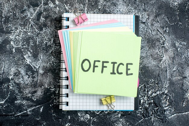 Draufsicht Büro geschriebene Notiz mit bunten Aufklebern und Heft auf grauem Hintergrund