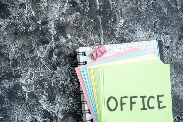 Draufsicht Büro geschriebene Notiz mit bunten Aufklebern und Heft auf grauem Hintergrund