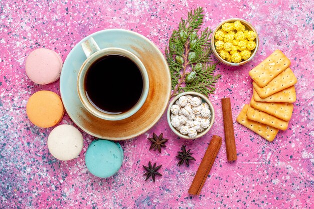 Draufsicht bunte französische Macarons der Ansicht mit Zimtcrackern und Tasse Tee auf rosa Schreibtisch backen Kuchen süße Zuckerkuchenfarbe