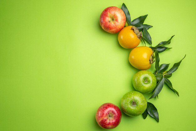 Draufsicht bunte Früchte bunte Äpfel Kakiblätter auf dem grünen Tisch