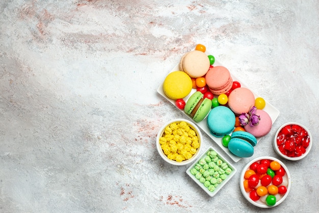 Kostenloses Foto draufsicht bunte köstliche macarons kleine kuchen mit bonbons auf hellem weißraum