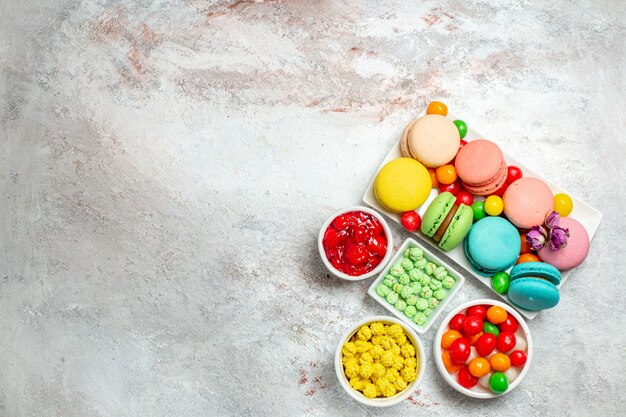 Draufsicht bunte köstliche Macarons kleine Kuchen mit Bonbons auf weißem Schreibtisch