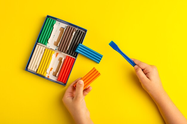 Draufsicht buntes Plastilinkind, das mit ihm auf gelber Wandfarbfoto-Kinderschule arbeitet und spielt