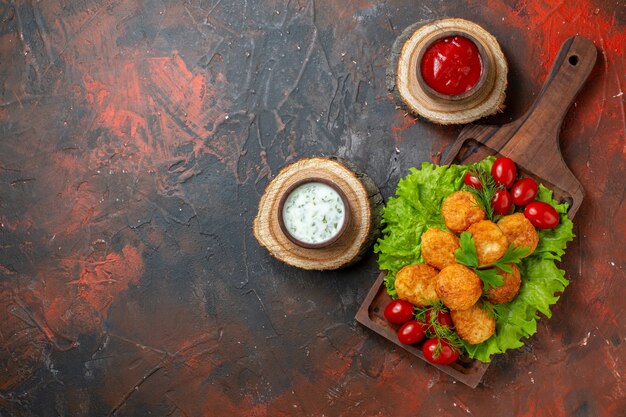 Draufsicht Chicken Nuggets Salat Kirschtomaten auf Holzbrett Saucen in Schalen auf Holzbrettern auf dunklem Tisch Freiraum