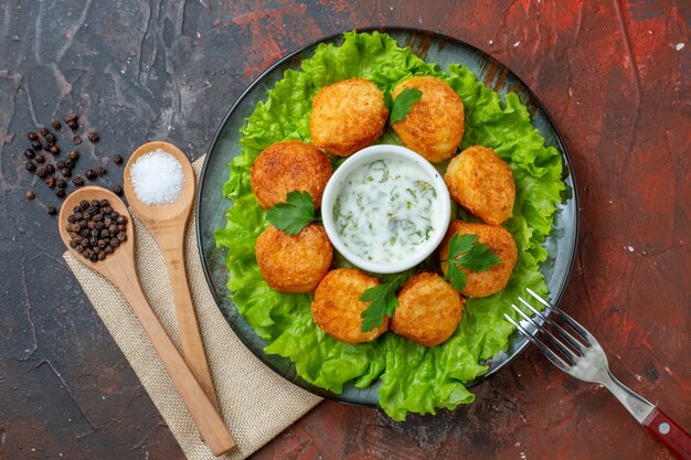 Draufsicht Chicken Nuggets Salatgabel auf Teller Salz und schwarzer Pfeffer in Holzlöffeln auf dunklem Tisch