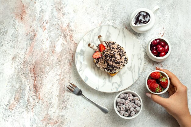 Draufsicht cremiger leckerer Kuchen mit Erdbeeren und Bonbons auf weißer Oberfläche Geburtstagscremeteekuchen Keks süß