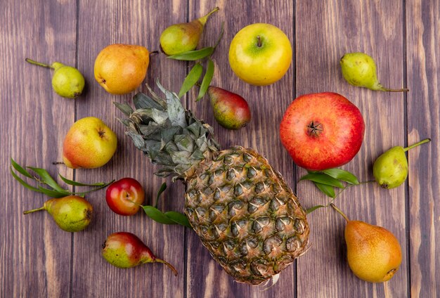 Draufsicht der Ananas mit Apfel-Pfirsich-Pflaumen-Granatapfel auf Holzoberfläche