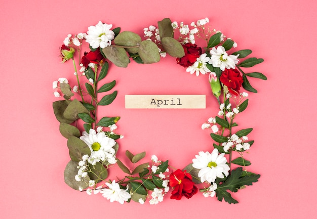 Draufsicht der April-Textmitte des bunten Blumenkranzes gegen Pfirsichoberfläche