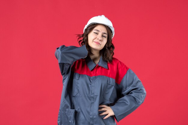 Draufsicht der Baumeisterin in Uniform mit Schutzhelm und Kopfschmerzen auf isoliertem rotem Hintergrund