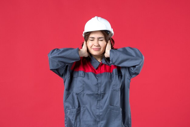 Draufsicht der Baumeisterin in Uniform mit Schutzhelm und nervös auf isoliertem rotem Hintergrund