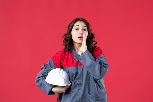 Draufsicht der Baumeisterin in Uniform und mit Schutzhelm, die jemanden auf isoliertem rotem Hintergrund anruft