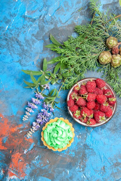 Draufsicht der Beerenschale, der kleinen Torte und der Äste auf der blauen Oberfläche