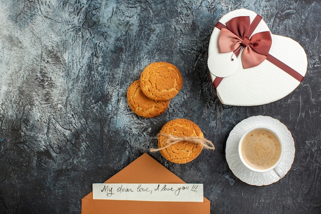 Draufsicht der besten überraschung mit schönem geschenkboxen-umschlag mit brief eine tasse kaffeekekse für geliebte auf der linken seite auf eisigem dunklem hintergrund