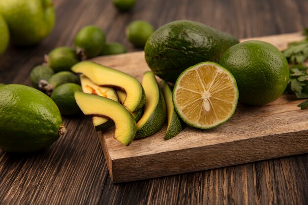 Draufsicht der birnenförmigen Avocado mit Scheiben auf einem hölzernen Küchenbrett mit Feijoas-Limetten lokalisiert auf einem hölzernen Hintergrund