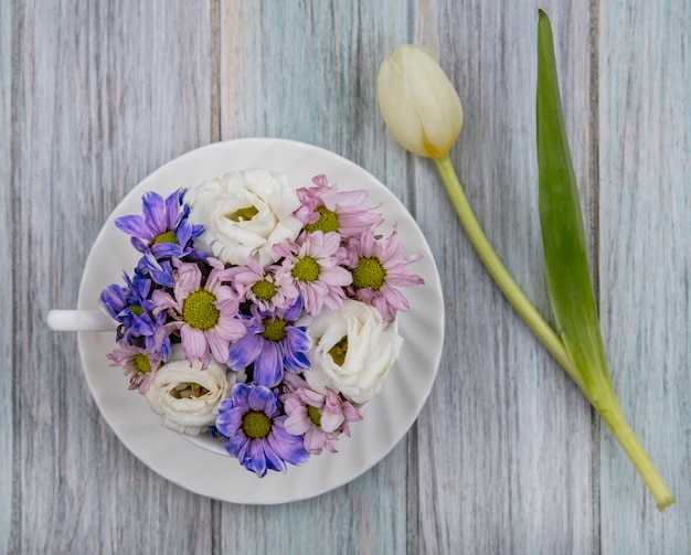 Draufsicht der Blumen in der Tasse auf Untertasse und auf hölzernem Hintergrund