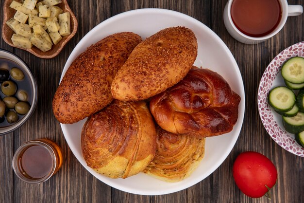 Draufsicht der Brötchen auf einem Teller mit Honig mit Olivengemüse und gehackten Käsescheiben auf einem hölzernen Hintergrund