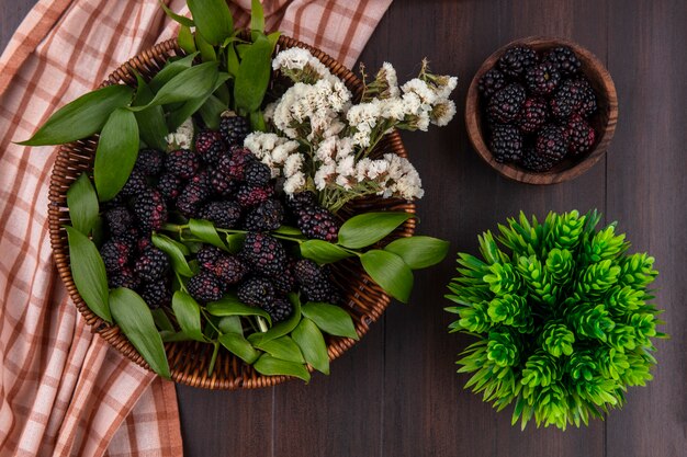 Draufsicht der Brombeere mit weißen Blumen in einem Korb mit einem karierten Zimthandtuch auf einer Holzoberfläche