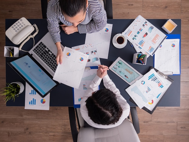 Draufsicht der Büroangestellten, die Finanzdiagramme analysieren, die Zwischenablage halten