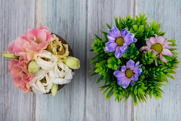 Draufsicht der bunten erstaunlichen Blumen auf einer hölzernen Schüssel mit Gänseblümchenblumen auf einem grauen hölzernen Hintergrund