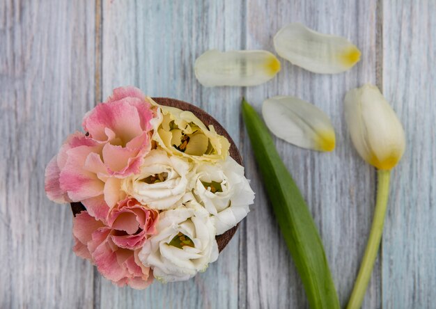 Draufsicht der bunten reizenden Blumen auf einer hölzernen Schüssel auf einem grauen hölzernen Hintergrund