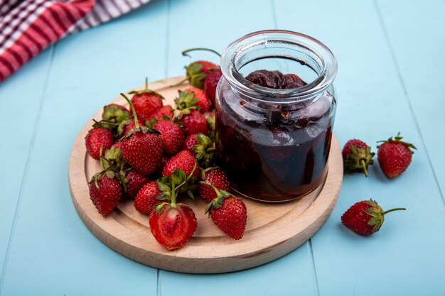 Draufsicht der Erdbeermarmelade mit frischen Erdbeeren auf einem hölzernen Küchenbrett auf einem blauen Hintergrund